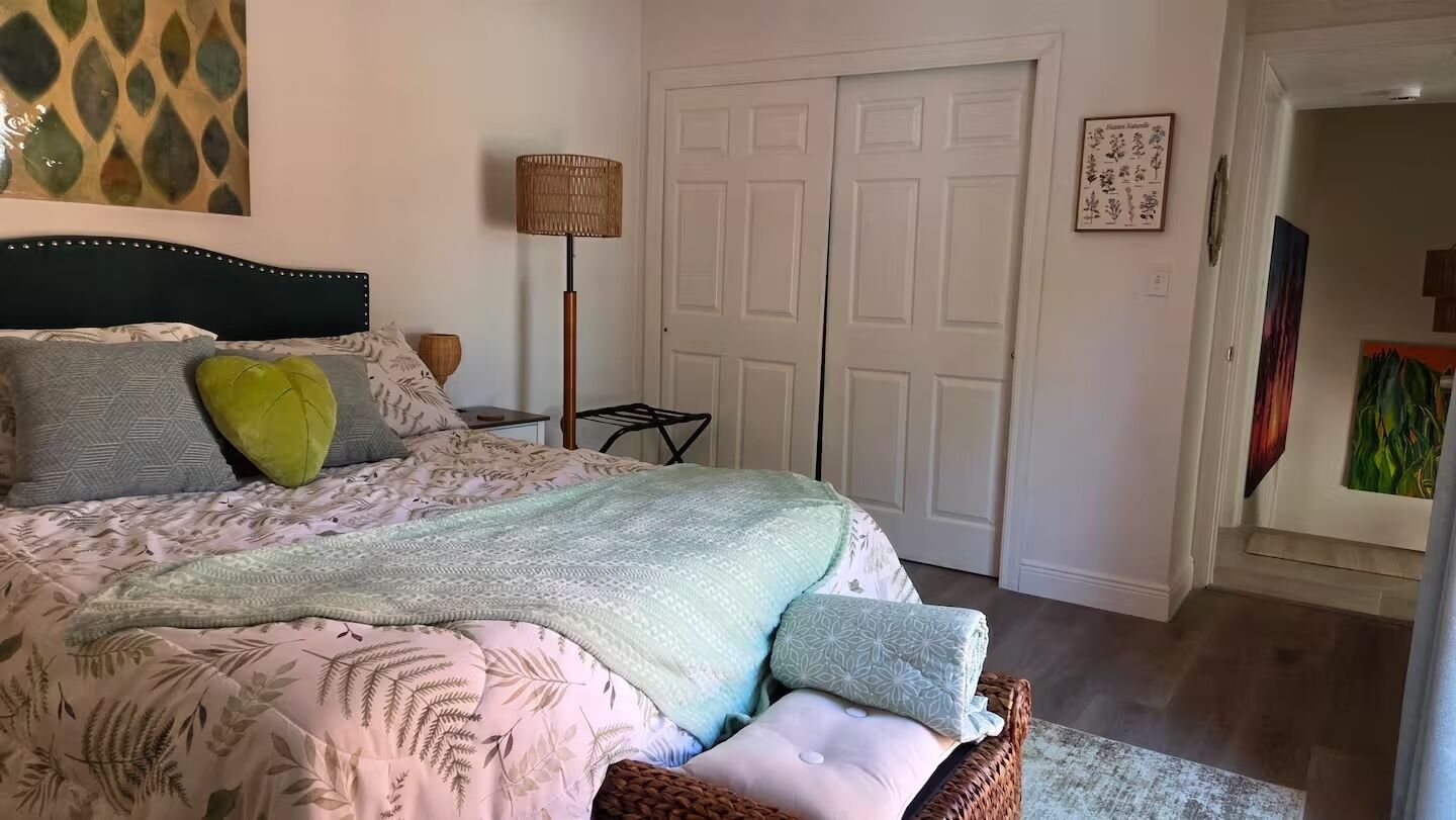 Una camera da letto con un letto, una lampada da comodino, una porta e una parete decorata con un'illustrazione botanica incorniciata.