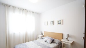 Ein Schlafzimmer mit einem Bett, zwei Nachttischen, einem Fenster mit Vorhängen und drei Wandbildern.