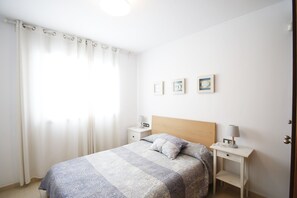 A bedroom with a bed, two bedside tables, a nightstand, a window with curtains, and three wall-mounted pictures. - Apartment Panoramic 23 by Parc Mont-roig (Miami Playa)