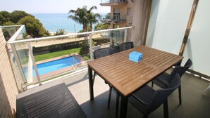 Ein Balkon mit Holztisch und -stühlen mit Blick auf einen Pool und das Meer.