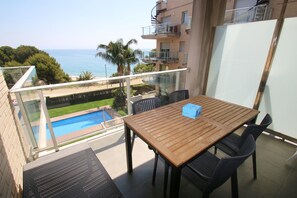 A balcony with a wooden table and chairs, overlooking a swimming pool and the sea. - Apartment Panoramic 23 by Parc Mont-roig (Miami Playa)