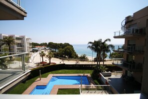 Zona de piscina con vistas a la playa y al océano, rodeada de edificios.