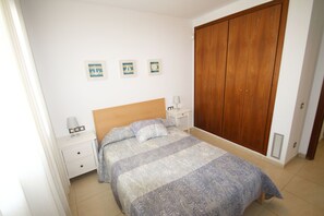 Un dormitorio con cama, mesitas de noche, un armario de madera y tres cuadros colgados en la pared.
