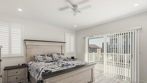 Een slaapkamer met een bed, nachtkastjes, een plafondventilator en uitzicht door een raam met jaloezieën.