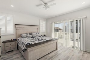 Ein Schlafzimmer mit einem Bett, Nachttischen, einem Deckenventilator und Blick durch ein Fenster mit Jalousien.