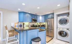 A modern kitchen with blue cabinets, stainless steel appliances, and a built-in washer and dryer.