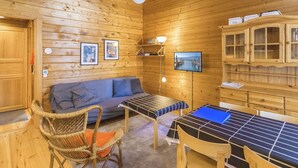 A wooden cabin interior with a sofa, chairs, a table, a TV, and wooden cabinets.