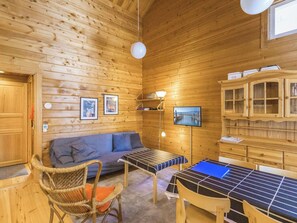 Interior de una cabaña de madera con sofá, sillas, una mesa, televisor y armarios de madera.