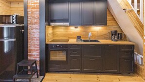 A compact kitchen with dark cabinets, a stainless steel refrigerator, and a wooden countertop.