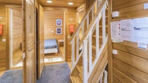 A wooden interior with a staircase, a bed, and informational posters on the walls.