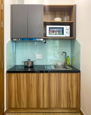 Una cocina compacta con microondas, una olla en la estufa, un lavabo y una repisa sobre la encimera.