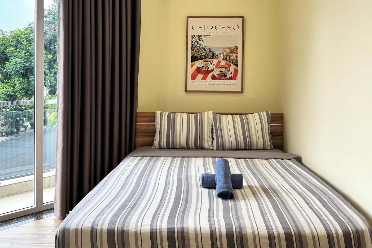 Una habitación de hotel con un ventanal grande, una cama con ropa de cama a rayas, un almohadón y un cartel en la pared.