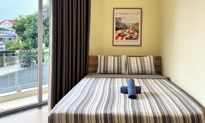 Una habitación de hotel con un ventanal grande, una cama con ropa de cama a rayas, un almohadón y un cartel en la pared.