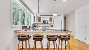 Een moderne keuken met een centraal eiland, krukken en hanglampen.