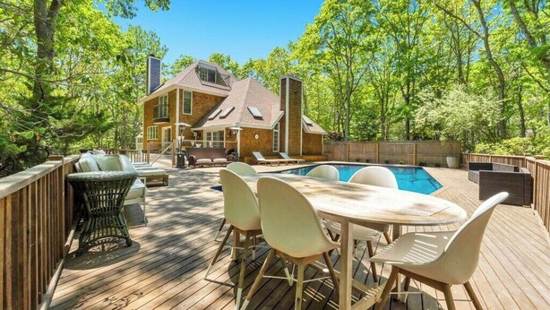 Eine Holzterrasse mit Pool, Gartenmöbeln und einem Haus im Hintergrund.