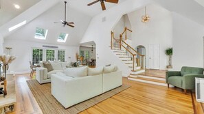 Un loft spacieux avec un plafond haut, des fenêtres de toit, un escalier et un grand canapé blanc.