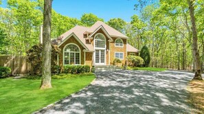 Une maison à deux étages avec une allée menant à la porte d’entrée, entourée d’arbres et d’une pelouse bien entretenue.