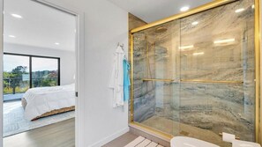 A modern bathroom with a glass-enclosed shower, a toilet, and a visible bed with a white bedspread. - Contemporary Shinnecock Hills Estate: Saltwater Heated Pool, Perfect Escape... (Southampton)