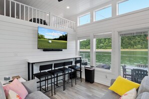 A room with a TV, bar area, seating, and a view of a body of water. - Tequila Sunrise - Relaxing Getaway Lake Cumberland (Russell Springs)