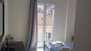 Een slaapkamer met een bed, een kleine tafel met een theepot, een raam met gordijnen en een airconditioning.