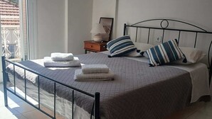 Een slaapkamer met een bed, kussens, een nachtkastje, een lamp en uitzicht op het exterieur.