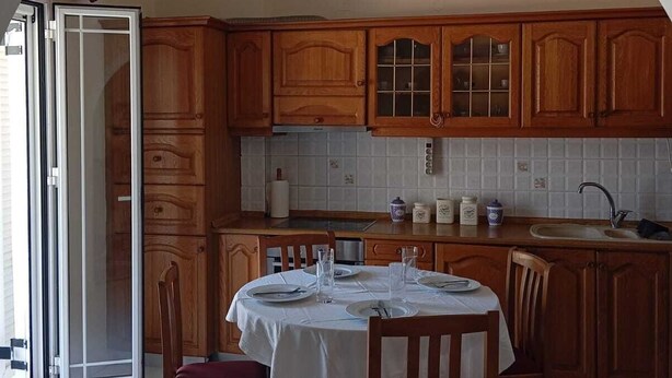 Een keuken met houten kastjes, een eettafel gedekt voor vier personen en een groot raam.