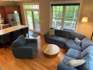 Un salon moderne comprenant un canapé d’angle, une table basse et un coin cuisine avec un réfrigérateur et une cuisinière.