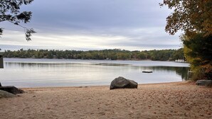 A lakeside view with a sandy beach, large rocks, and a distant shoreline. - Welcome to the Bear’s Den. A Delightful house on Lake Winnipesaukee in Meredith. (Meredith)