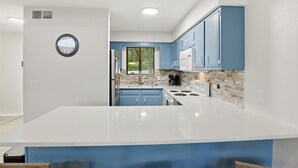 A modern kitchen with blue cabinets, a white countertop, and a stone backsplash.