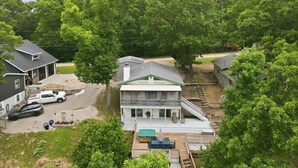 A two-story house with a covered deck, a driveway with parked cars, and a large green lawn.