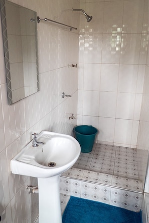 Un baño con lavamanos blanco, un espejo, ducha y una alfombra de baño azul.