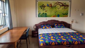 A bedroom with a bed, a desk, and a chair. There is a window with bars and a curtain.