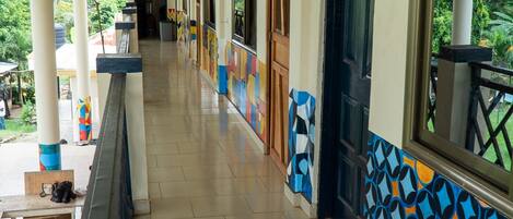 A covered corridor with tiled flooring, wooden doors, and windows with a view of greenery.