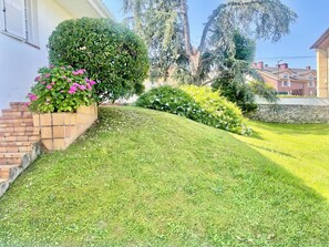 A well-maintained lawn, a brick planter with flowers, and a stone wall. - Casa Sierrapando - by Wehomes (Torrelavega)