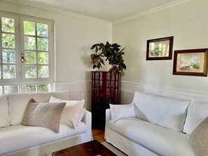 Une pièce comprenant deux canapés blancs, un grand présentoir à plantes en bois et deux œuvres d’art encadrées accrochées au mur.
