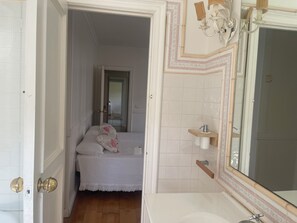 A bedroom with a bed, a bathroom with a sink and mirror, and a hallway leading to another room.