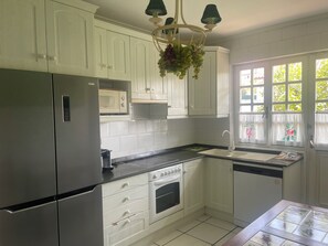 Een keuken met witte kasten, een roestvrijstalen koelkast, een magnetron, een fornuis en een raam met bloemen gordijnen.