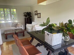 Een woonkamer met een witte bank, een salontafel, een eettafel met stoelen en een potplant.