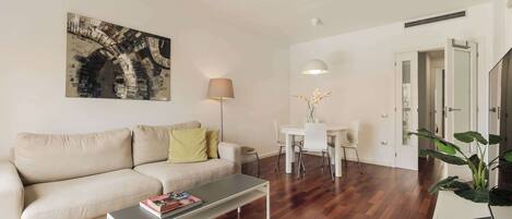 A modern living room with a sofa, coffee table, lamp, dining table, chairs, and a large painting.