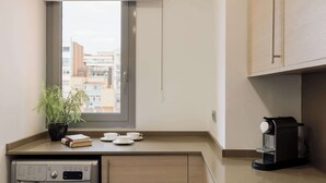 Eine kleine Küche mit Waschmaschine, Kaffeemaschine, einem Blumentopf und Blick auf Gebäude durch ein Fenster.