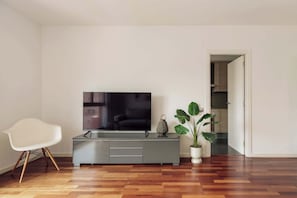 Un soggiorno moderno con televisione a schermo piatto, una poltrona bianca, un mobile grigio e una pianta in vaso.