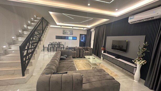Una sala de estar moderna con un sofá modular, un televisor de pantalla plana, una escalera y un comedor.