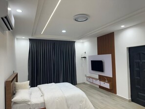 A modern bedroom with a bed, a TV mounted on the wall, and a door. - Monte Luxury Home (North Legon)