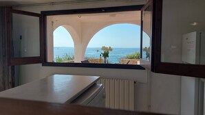 Een kamer met uitzicht op de zee, zichtbaar door een open raam, met een stenen muur en een radiator.