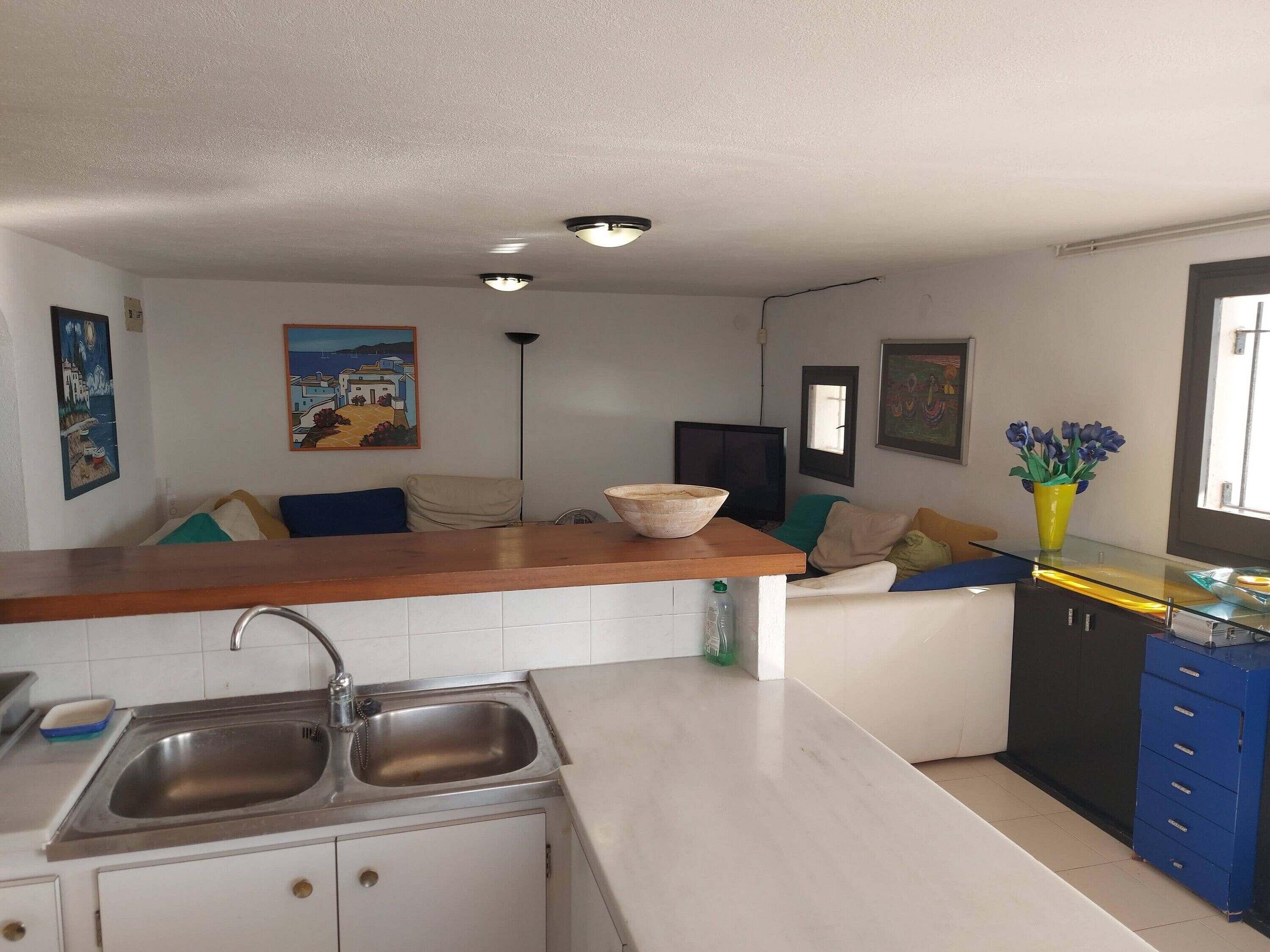 A modern kitchen with a wooden countertop, stainless steel sink, and a dining area with a sofa and a TV.