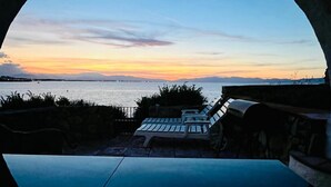 Rond raam met uitzicht op een zonsondergang, met lounge stoelen en een tafel.