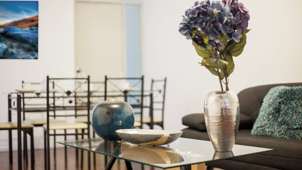 A modern living room with a glass coffee table, a vase with flowers, and a painting on the wall. - Enjoyable 2-bedroom apartment with AC in Miraflores neighborhood (Miraflores)
