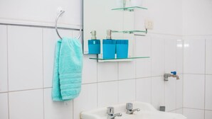 A bathroom with a white sink, two faucets, a towel rack with a blue towel, and two blue bottles on a glass shelf above the sink. - Enjoyable 2-bedroom apartment with AC in Miraflores neighborhood (Miraflores)