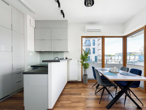 A modern kitchen with white cabinets, a central island, and a dining area with a table and chairs. - Apartment Novum by Interhome (Krakow)