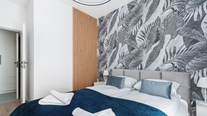 Un dormitorio moderno con cama, pared de madera y papel tapiz con motivos de hojas tropicales.